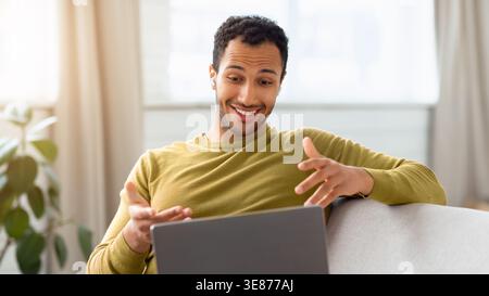Man Sits on Sofa and Talks While Using Laptop at Home in Daylight Stock Photo