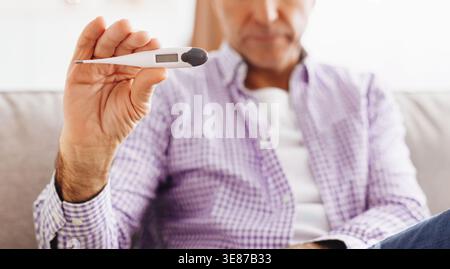 Man Measures Temperature While Sitting on Couch at Home During Daytime Stock Photo