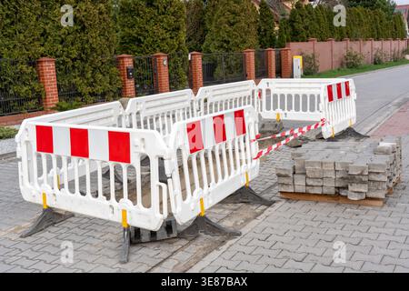 Road construction site with white plastic safety barriers and red warning tape blocking damaged pavement hole on residential street. Urban Stock Photo
