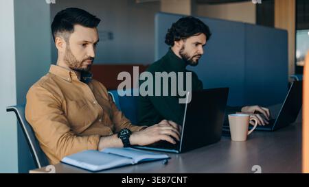 Two Men Working on Laptops in a Modern Office Space During the Day Stock Photo