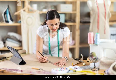 Woman dressmaker makes pattern using drawing on tablet Stock Photo
