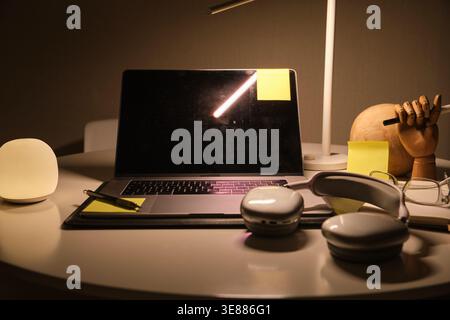 Study area with laptop, headphones, desk lamp, and sticky notes for remote work Stock Photo