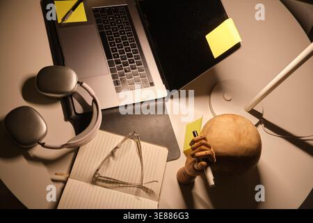 Workspace featuring a laptop, headphones, notebook, glasses, and desk lamp, creating a focused environment Stock Photo