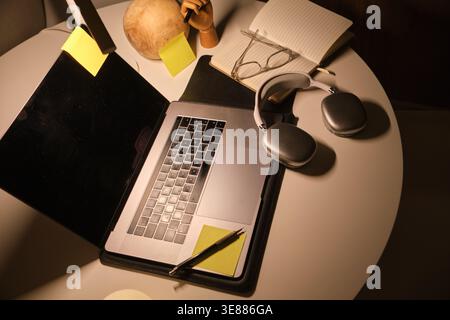 Study area with laptop, headphones, glasses, and notebook on a white table Stock Photo