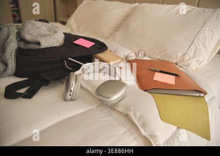 Student belongings and school supplies resting on a clean white bed, creating a study area Stock Photo