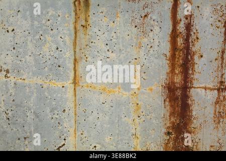 Close-up of long brownish rust streaks, yellow orange stains and small holes on old light greyish blue painted concrete wall surface in poor and damag Stock Photo