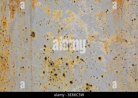 Close-up of brownish rust streaks, yellow orange stains and small holes on old light greyish blue painted concrete wall surface in poor and damaged co Stock Photo