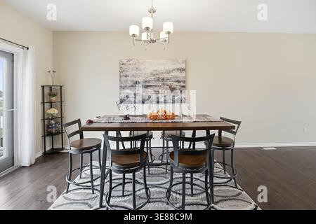 Cozy dining room with warm wood tones and elegant chandelier. Modern table seats six with rustic black metal chairs. Artwork hangs above, adding sophi Stock Photo