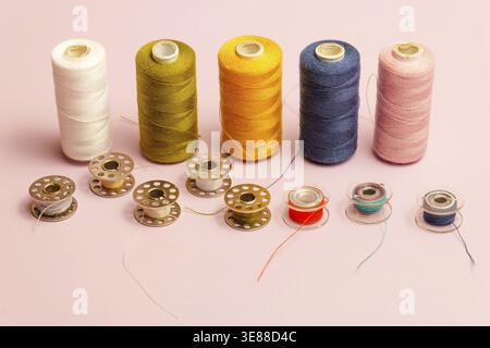 Various large thread spools and smaller bobbins displaying a range of colors, including white, green, yellow, blue, and pink, are neatly organized on Stock Photo