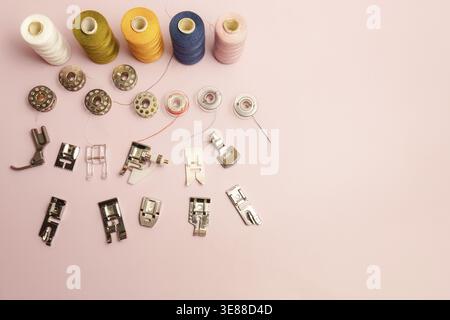 Sewing accessories including bobbins. Presser feet. And various spools of colorful thread are neatly arranged on a light pink surface. Symbolizing cra Stock Photo