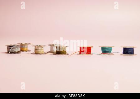 Row of colorful sewing thread bobbins, including shades of blue, green, orange, white, gold, and grey, creating a vibrant display for craft and textil Stock Photo