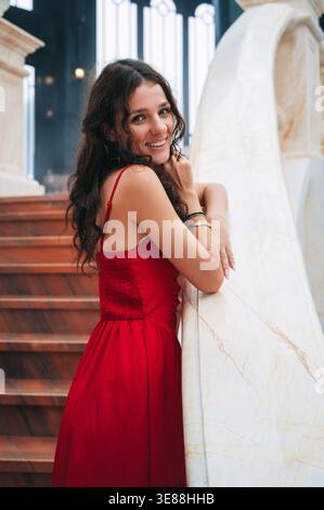 A romantic princess stands gracefully in a red dress inside an ancient castle. Stock Photo