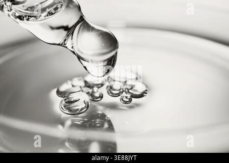 Dropper releases transparent liquid forming small bubbles on reflective surface Stock Photo