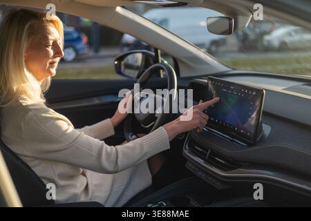 Automotive engineer using a digital touchscreen interface while seated in a contemporary vehicle. Natural light enhances the sleek dashboard design, with various controls visible. Stock Photo