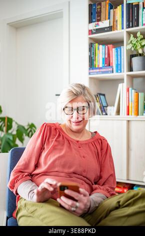 Older woman scrolling on phone while working from home during retirement. Stock Photo