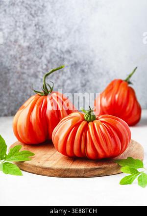 Fresh heirloom "Coeur de Boeuf" Aurea tomatoes on a wooden board. Ribbed Oxheart beefsteak tomatoes (Solanum lycopersicum) Stock Photo