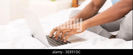 African-american programmer typing on laptop in bed Stock Photo