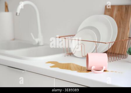 Overturned cup and spilled coffee on counter in kitchen Stock Photo