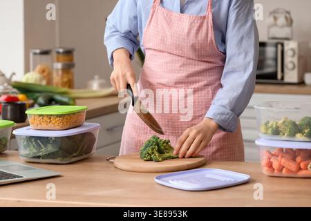 Woman cutting broccoli for freezing on wooden table in kitchen Stock Photo