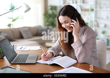 Happy teleworker writing in agenda making phone call working at home Stock Photo