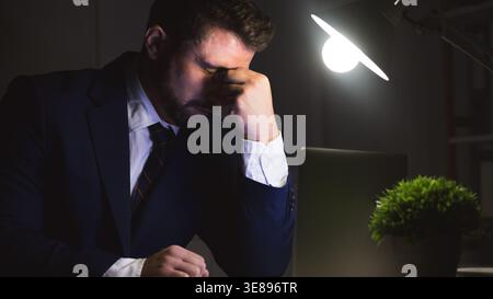 Exhausted businessman doing report on laptop, having problems Stock Photo