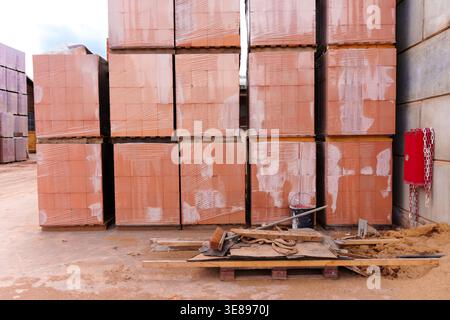Orange clay bricks sit stacked on wooden pallets and wrapped in protective plastic film at a building material yard in Hainstadt, Germany, waiting for Stock Photo