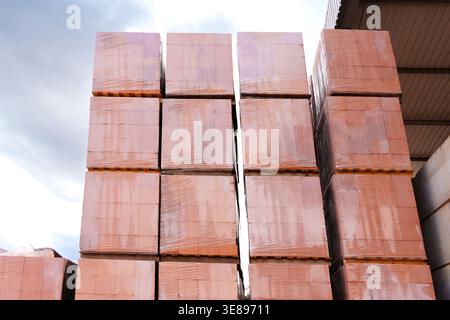 Neatly stacked red clay building bricks are packed on wooden pallets and secured with plastic wrapping for transportation from a manufacturing facilit Stock Photo