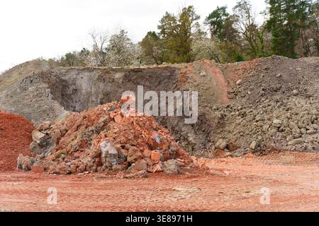 Large mounds of red clay and gray excavated soil are processed at an industrial excavation site in Hainstadt, Germany, highlighting various geological Stock Photo