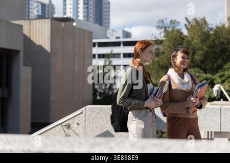 Diverse female students walking, talking on campus holding books backpacks near parapet, copy space Stock Photo