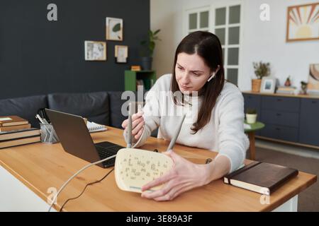 Caucasian young adult woman connecting router cable beside laptop, troubleshooting home internet setup for remote work and digital access. Usable for broadband service or tech support ads Stock Photo