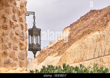Vintage oriental metal lantern mounted on rustic stone wall. Authentic Middle Eastern decor creating Arabian Nights atmosphere in desert landscape. Stock Photo