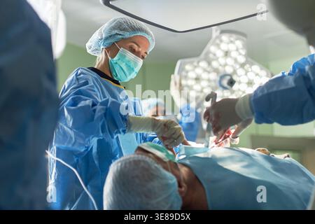 Low angle view of female surgeon performing operation with medical team in operating room, representing healthcare precision and emergency treatment. Useful for hospital care marketing Stock Photo