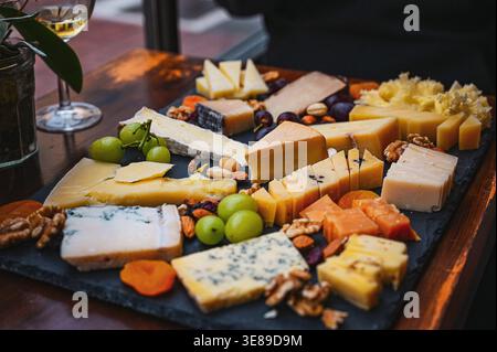 Assorted cheese board with grapes, nuts and dried fruit served on a slate platter in a restaurant setting. Stock Photo