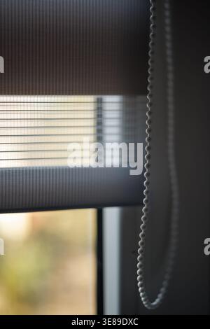 Modern zebra-pattern roller blinds with a ball-shaped cord for raising or lowering. Close-up, focusing on the cord. Focus on the foreground. Stock Photo