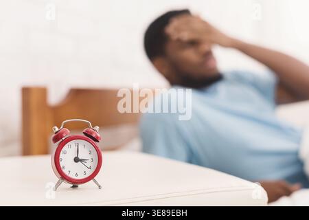 Man Sitting on a Bed With His Hand on His Forehead While a Clock Shows Morning Time Stock Photo