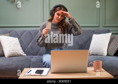 Young woman is sitting on bed in living room and having online doctor's appointment using laptop. Young woman taking medication while working on lapto Stock Photo