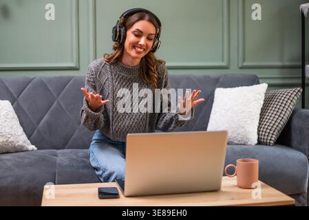 Woman having a joyful conversation on her laptop, sharing laughs and staying connected through the internet from the comfort of her home. Stock Photo