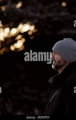 Profile of a smiling man with a beard wearing a gray beanie outdoors Stock Photo
