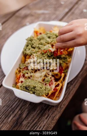 Hand picking nachos with melted cheese and guacamole Stock Photo