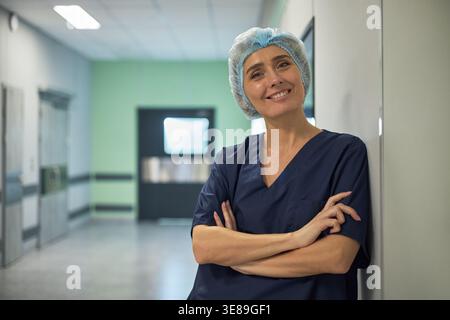 Portrait of middle aged Caucasian female healthcare worker standing with crossed arms in hospital corridor, conveying confidence and professionalism. For medical staffing or clinic promotion Stock Photo