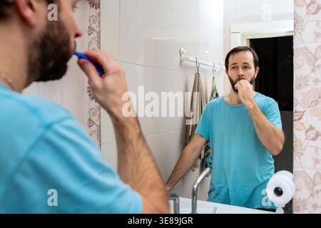 Man brushing tooth in bathroom looking at mirror reflection. Stock Photo
