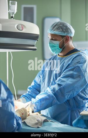 Vertical shot of middle aged Caucasian male surgeon performing operation in hospital operating room, representing healthcare expertise and surgical care. Useful for medical services marketing Stock Photo