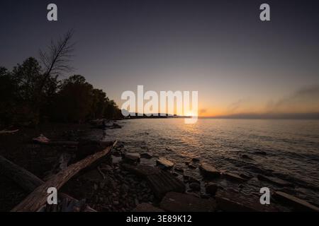 Sunset reflecting on lake water with shore and trees Stock Photo