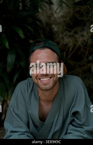 Happy young man with earbuds and glasses smiling in tropical garden Stock Photo