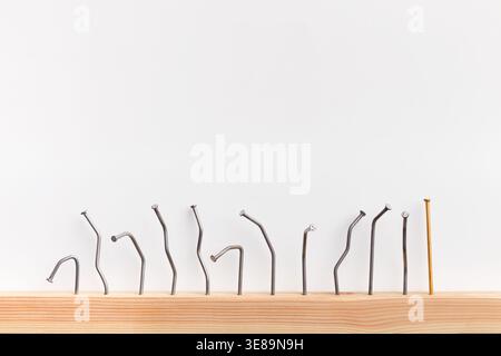 Collection of Bent and Straight Nails Arranged on a Wooden Surface Set Against a Plain Background Stock Photo
