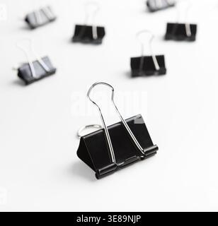 Collection of Black Binder Clips Arranged on a White Surface With Focus on One Binder Clip Stock Photo