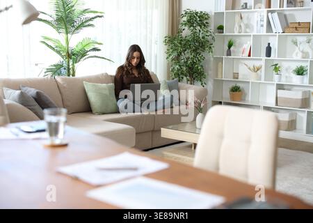 Woman preferring to work sitting on a couch rather than at the table teleworking at home Stock Photo