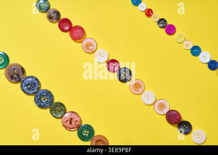 Colorful sewing buttons arranged in clean diagonal lines on yellow background creating modern minimal pattern Stock Photo