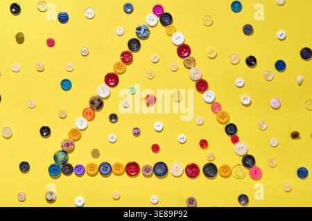 Geometric triangle composition made of various sewing buttons on a bright yellow background. Creative layout Stock Photo