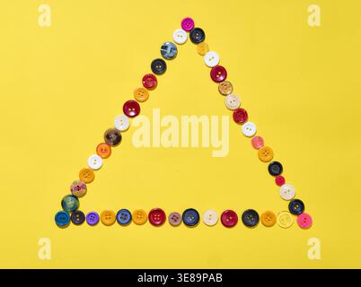 Geometric triangle composition made of various sewing buttons on a bright yellow background. Creative layout Stock Photo